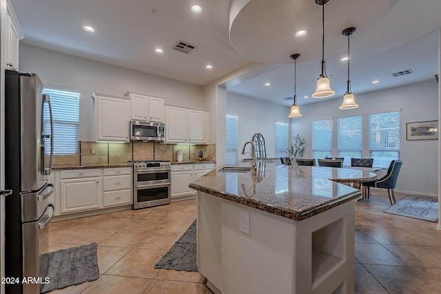 kitchen with white cabinets, appliances with stainless steel finishes, dark stone counters, and a center island with sink