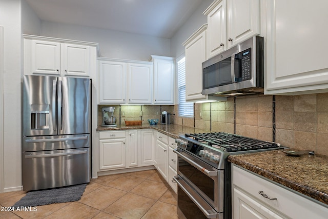 kitchen with white cabinetry, appliances with stainless steel finishes, dark stone counters, light tile patterned floors, and decorative backsplash