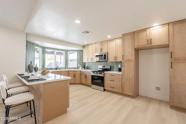 1609 W Yukon Dr, Phoenix, AZ 85027 - kitchen featuring stainless steel appliances, light brown cabinets, light wood-style floors, a peninsula, and a kitchen bar