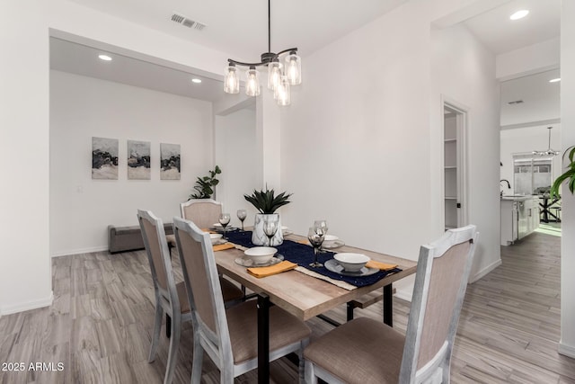 dining area with an inviting chandelier, sink, and light wood-type flooring