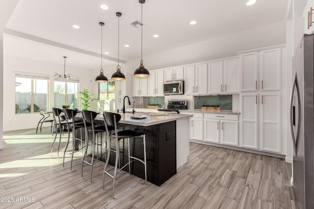 kitchen with decorative light fixtures, stainless steel appliances, an island with sink, and white cabinets