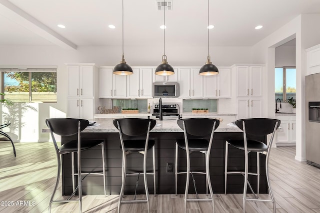 kitchen with tasteful backsplash, white cabinets, a large island, light stone counters, and stainless steel appliances