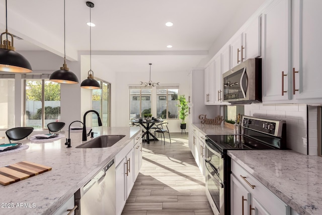 kitchen with tasteful backsplash, white cabinetry, sink, light stone counters, and stainless steel appliances