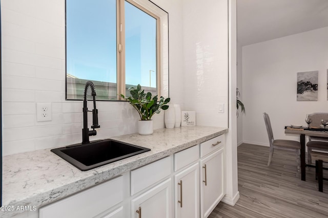 kitchen with light stone counters, sink, light hardwood / wood-style flooring, and white cabinets