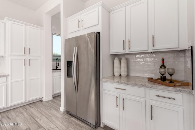 kitchen featuring white cabinetry, backsplash, stainless steel refrigerator with ice dispenser, light stone countertops, and light wood-type flooring