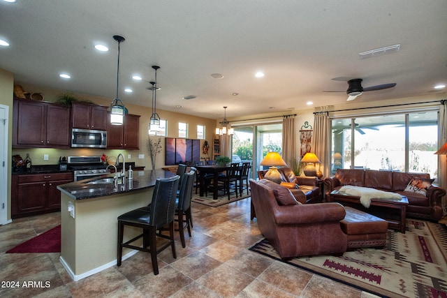 kitchen with pendant lighting, ceiling fan with notable chandelier, sink, an island with sink, and stainless steel appliances