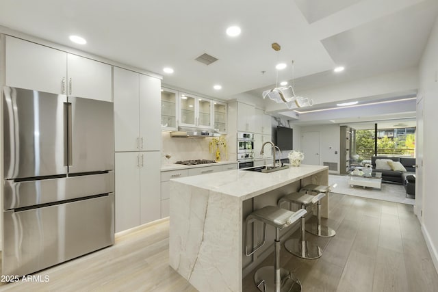 kitchen featuring sink, a breakfast bar area, white cabinetry, stainless steel appliances, and a kitchen island with sink