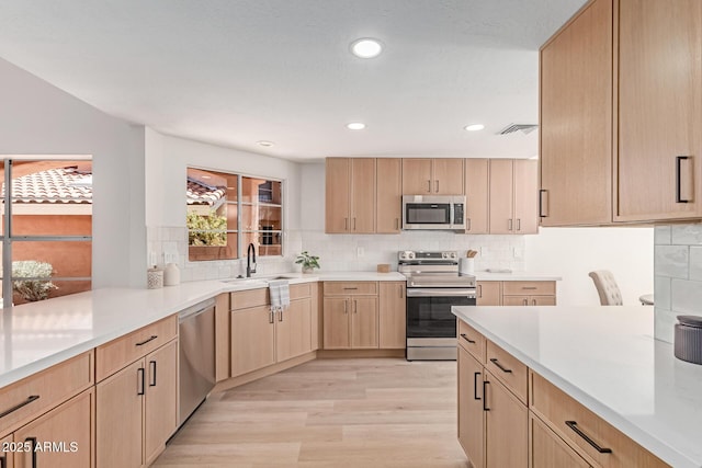 6439 E Redmont Dr, Mesa, AZ 85215 - kitchen with stainless steel appliances, light brown cabinetry, light wood-type flooring, tasteful backsplash, and light countertops