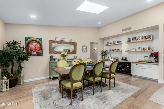 dining space with vaulted ceiling with skylight and light hardwood / wood-style flooring