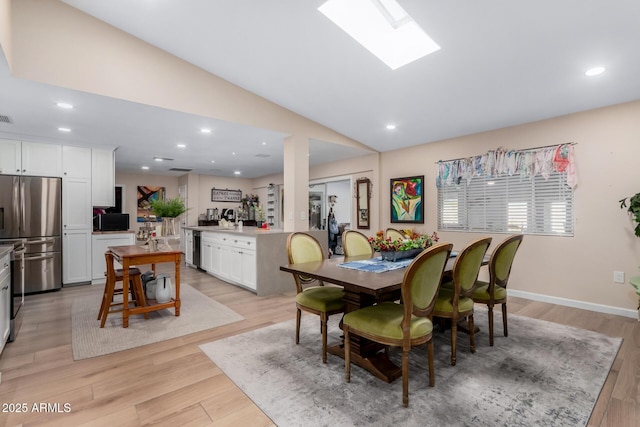 dining space with vaulted ceiling with skylight and light hardwood / wood-style flooring