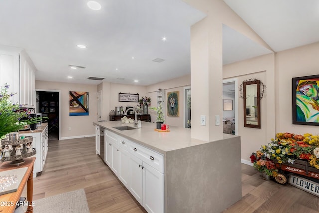 kitchen with sink, white cabinetry, stainless steel dishwasher, light hardwood / wood-style floors, and a kitchen island with sink