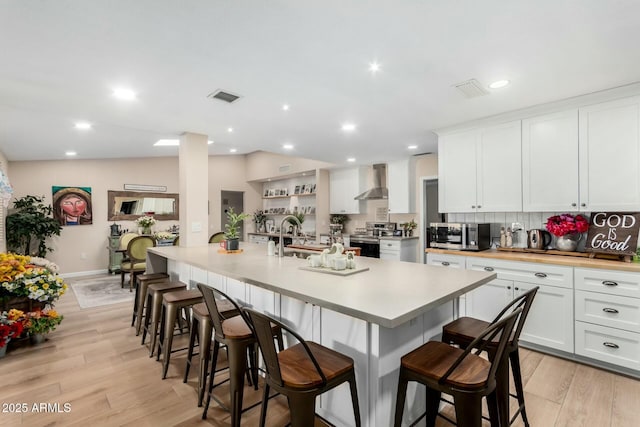 kitchen with a breakfast bar, appliances with stainless steel finishes, light hardwood / wood-style floors, white cabinets, and wall chimney exhaust hood