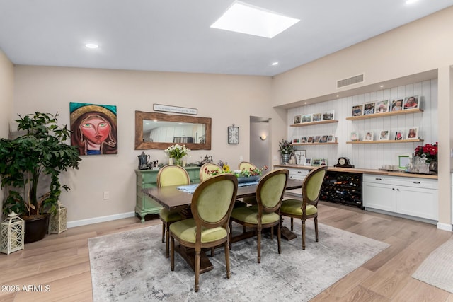 dining room featuring vaulted ceiling with skylight and light hardwood / wood-style floors