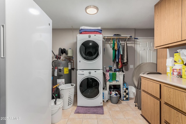 laundry area featuring cabinets, electric water heater, stacked washer / drying machine, and light tile patterned flooring