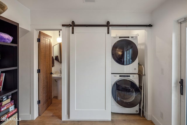 laundry area featuring stacked washer and dryer, a barn door, and light hardwood / wood-style floors