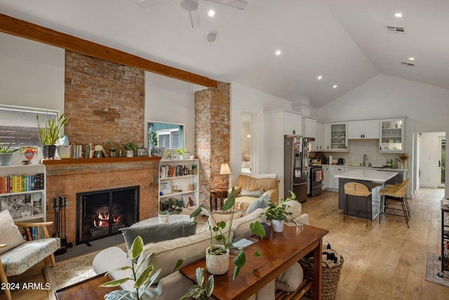 living room featuring a fireplace, high vaulted ceiling, sink, ceiling fan, and light hardwood / wood-style floors