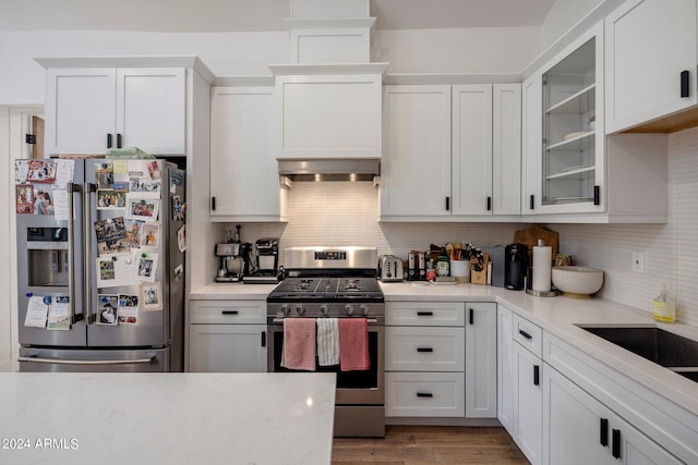 kitchen with light wood-type flooring, stainless steel appliances, range hood, decorative backsplash, and white cabinets