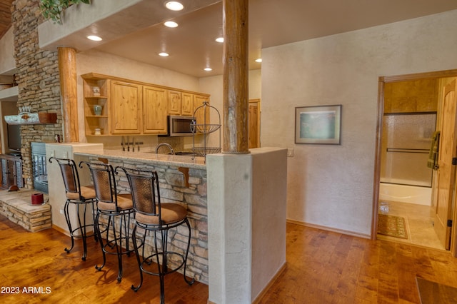 kitchen with open shelves, recessed lighting, stainless steel microwave, a kitchen bar, and hardwood / wood-style flooring