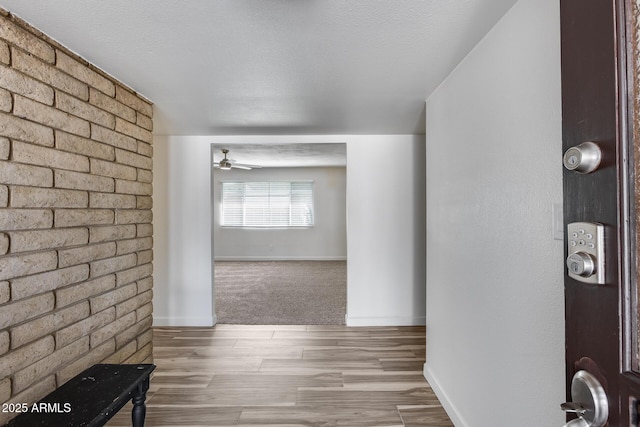 hall featuring a textured ceiling, baseboards, and wood finished floors