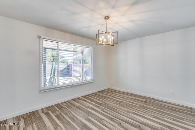 empty room featuring light wood-type flooring, baseboards, and a chandelier