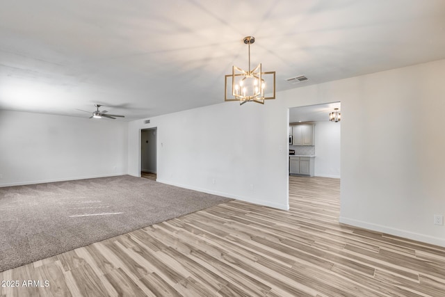 empty room with light wood-type flooring, visible vents, baseboards, and ceiling fan with notable chandelier