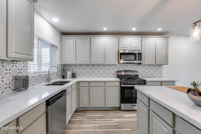 kitchen with light wood finished floors, tasteful backsplash, appliances with stainless steel finishes, light countertops, and a sink