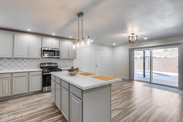 kitchen with stainless steel appliances, light countertops, a center island, light wood finished floors, and tasteful backsplash