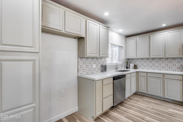 kitchen with tasteful backsplash, light countertops, stainless steel dishwasher, a sink, and light wood-type flooring