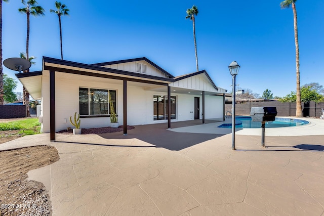 back of property with board and batten siding, a fenced in pool, a patio area, and fence