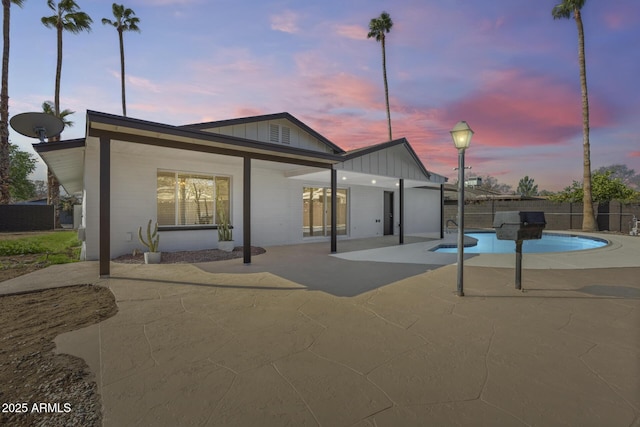 back of property at dusk with a fenced in pool, fence, board and batten siding, and a patio