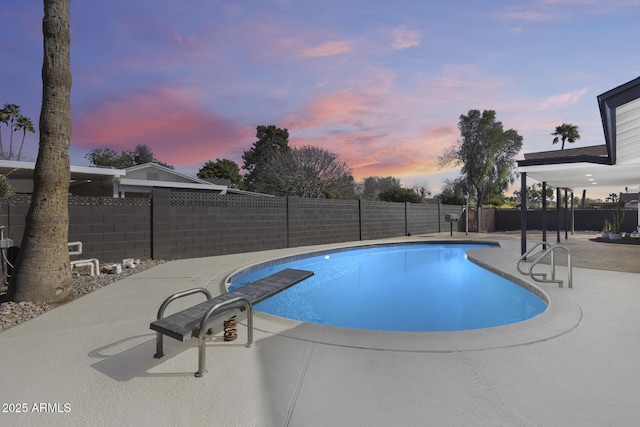 pool at dusk with a patio area, a fenced backyard, a diving board, and a fenced in pool