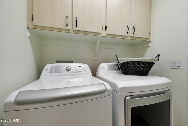 clothes washing area featuring washing machine and dryer, cabinet space, and a textured wall