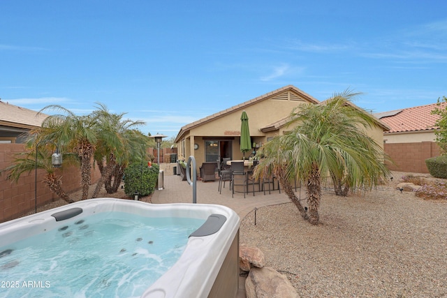 rear view of house with a patio, stucco siding, a fenced backyard, and a hot tub