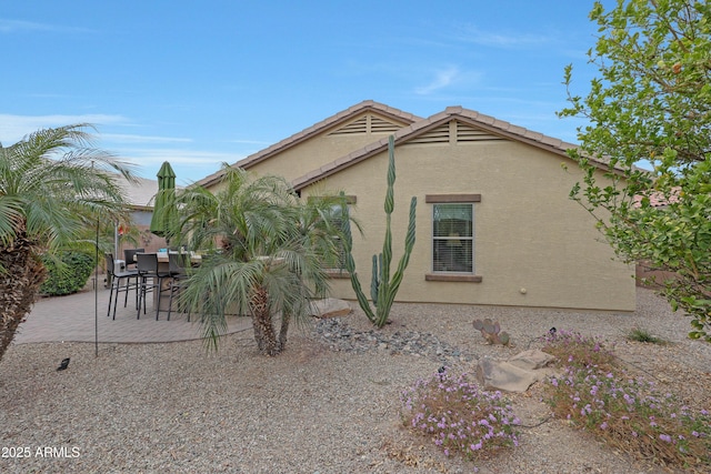 view of side of home featuring a patio area, a tile roof, and stucco siding