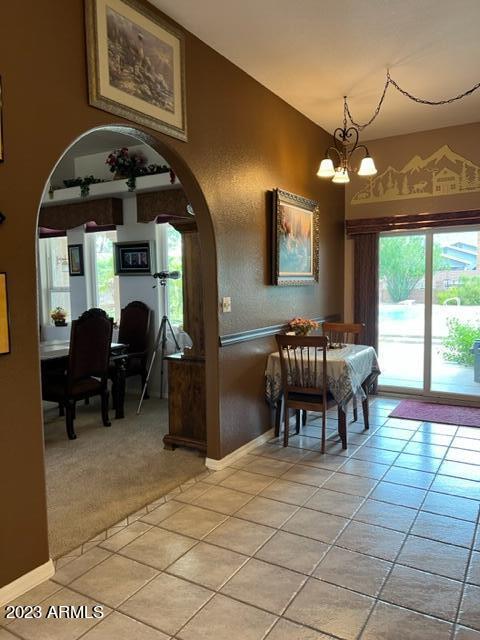 dining space with light tile patterned floors, arched walkways, a notable chandelier, and light colored carpet