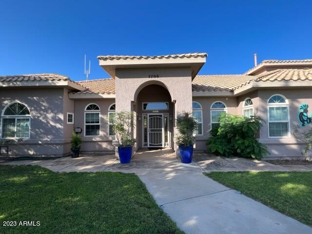 view of exterior entry with stucco siding, a tile roof, and a yard