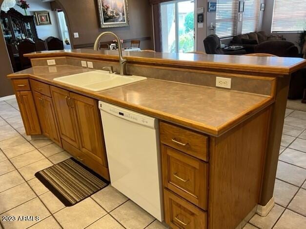 kitchen with arched walkways, dishwasher, an island with sink, brown cabinets, and a sink