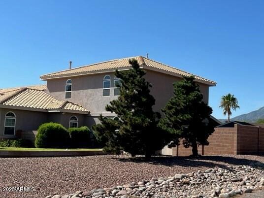 view of property exterior with fence, a tiled roof, and stucco siding