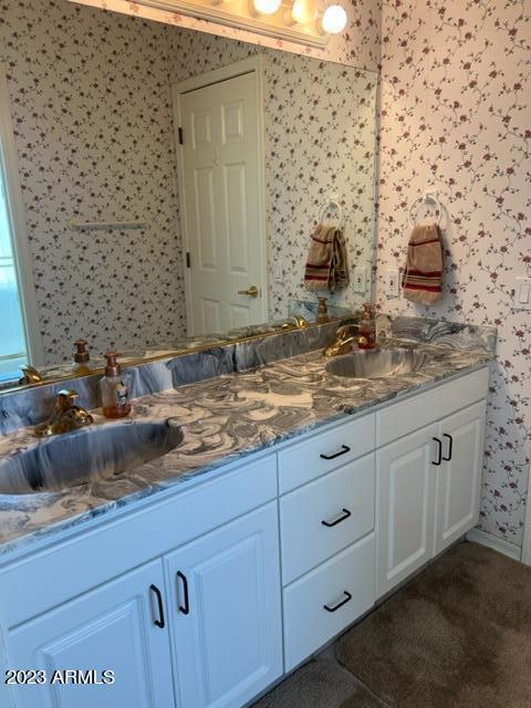 full bathroom featuring double vanity, wallpapered walls, and a sink