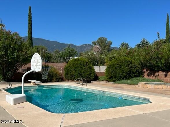 view of swimming pool with a hot tub, a fenced backyard, a mountain view, and a fenced in pool