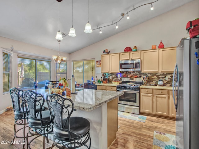 kitchen featuring a breakfast bar, decorative light fixtures, light brown cabinets, an island with sink, and stainless steel appliances