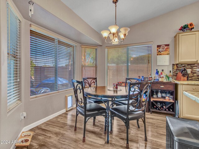 dining space with an inviting chandelier, vaulted ceiling, and light wood-type flooring