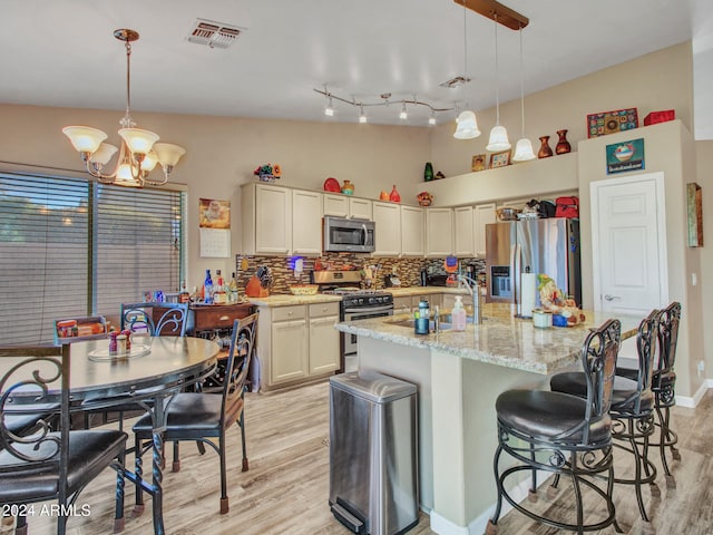 kitchen with tasteful backsplash, light stone counters, pendant lighting, stainless steel appliances, and a kitchen island with sink