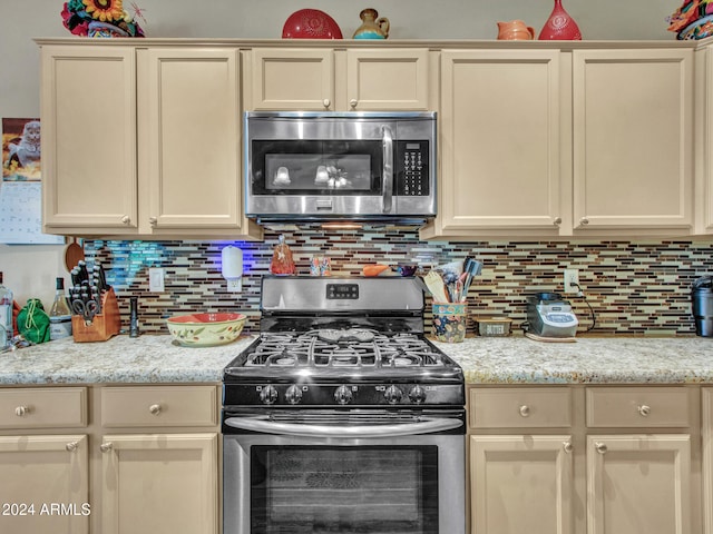 kitchen with stainless steel appliances, light stone countertops, cream cabinets, and backsplash