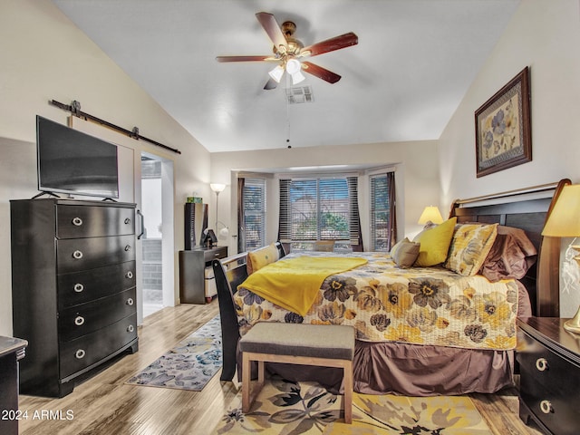 bedroom featuring vaulted ceiling, a barn door, ceiling fan, and light hardwood / wood-style flooring