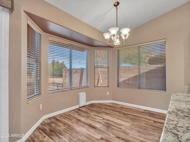 unfurnished dining area featuring hardwood / wood-style flooring, lofted ceiling, and an inviting chandelier