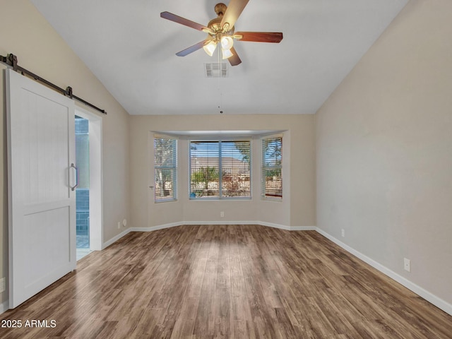 spare room featuring ceiling fan, lofted ceiling, a barn door, and wood-type flooring