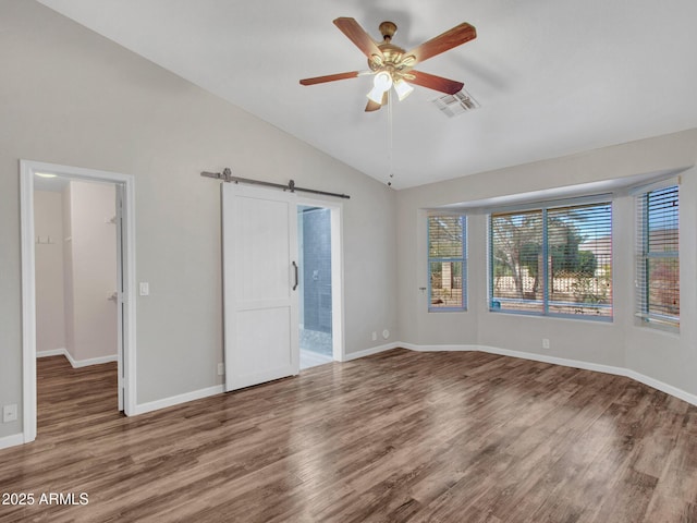 unfurnished bedroom featuring ensuite bath, ceiling fan, wood-type flooring, vaulted ceiling, and a barn door