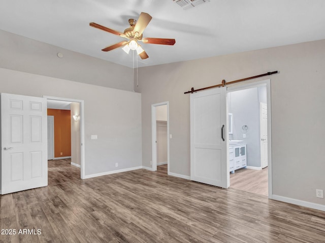 empty room with vaulted ceiling, a barn door, ceiling fan, and light hardwood / wood-style floors