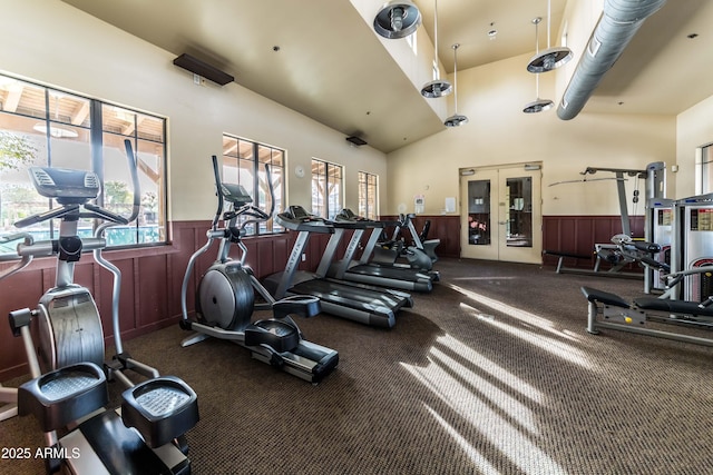 gym featuring french doors, a high ceiling, dark colored carpet, and wooden walls